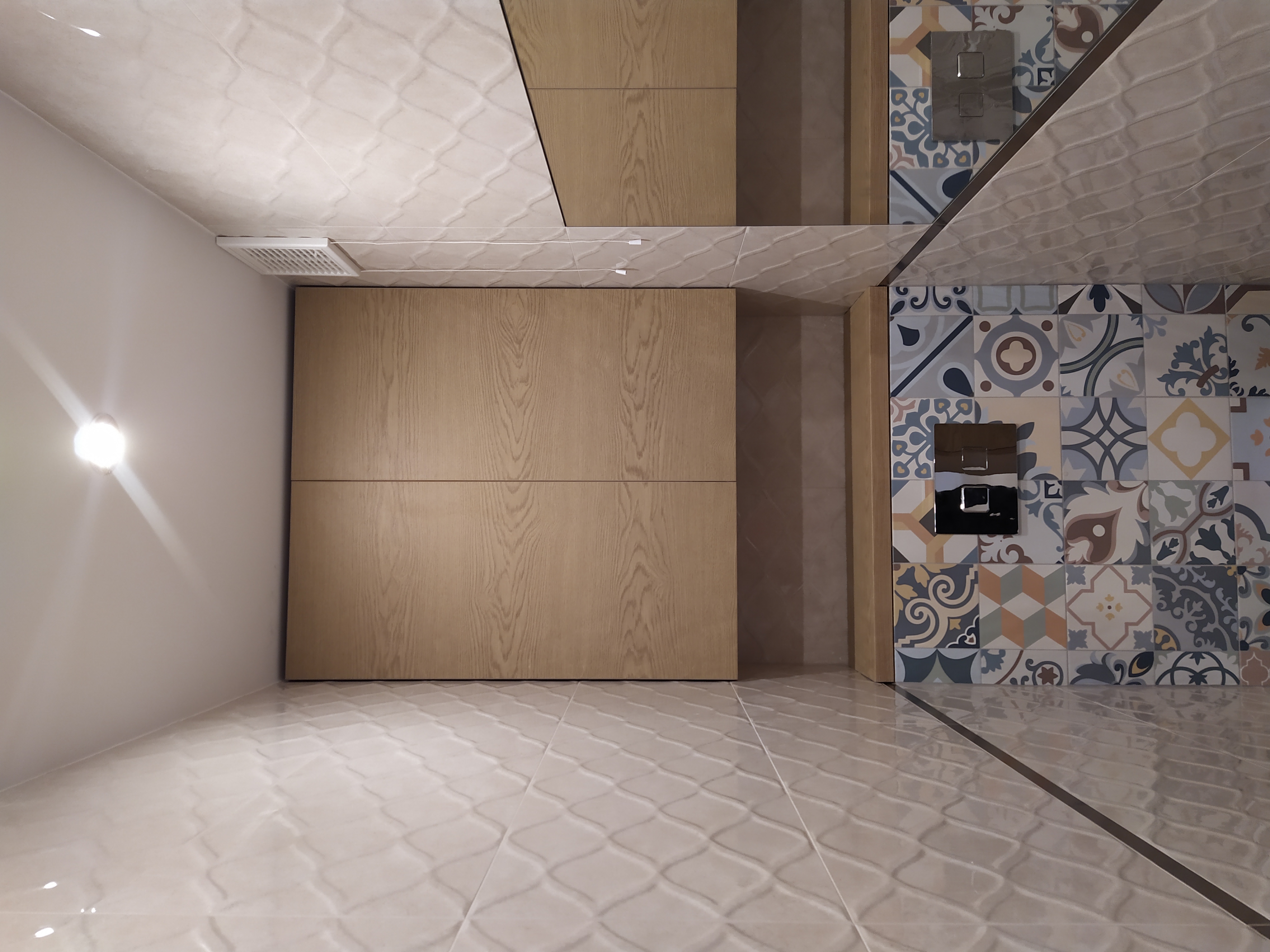 Nowoczesna kuchnia z drewnianymi frontami szafek bez uchwytów, patchworkowymi płytkami na ścianie i błyszczącą podłogą z reliefowym wzorem, widziana z perspektywy sufitu.