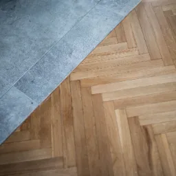 Połączenie szarej, matowej podłogi z płytek i parkietu ułożonego w jodełkę.