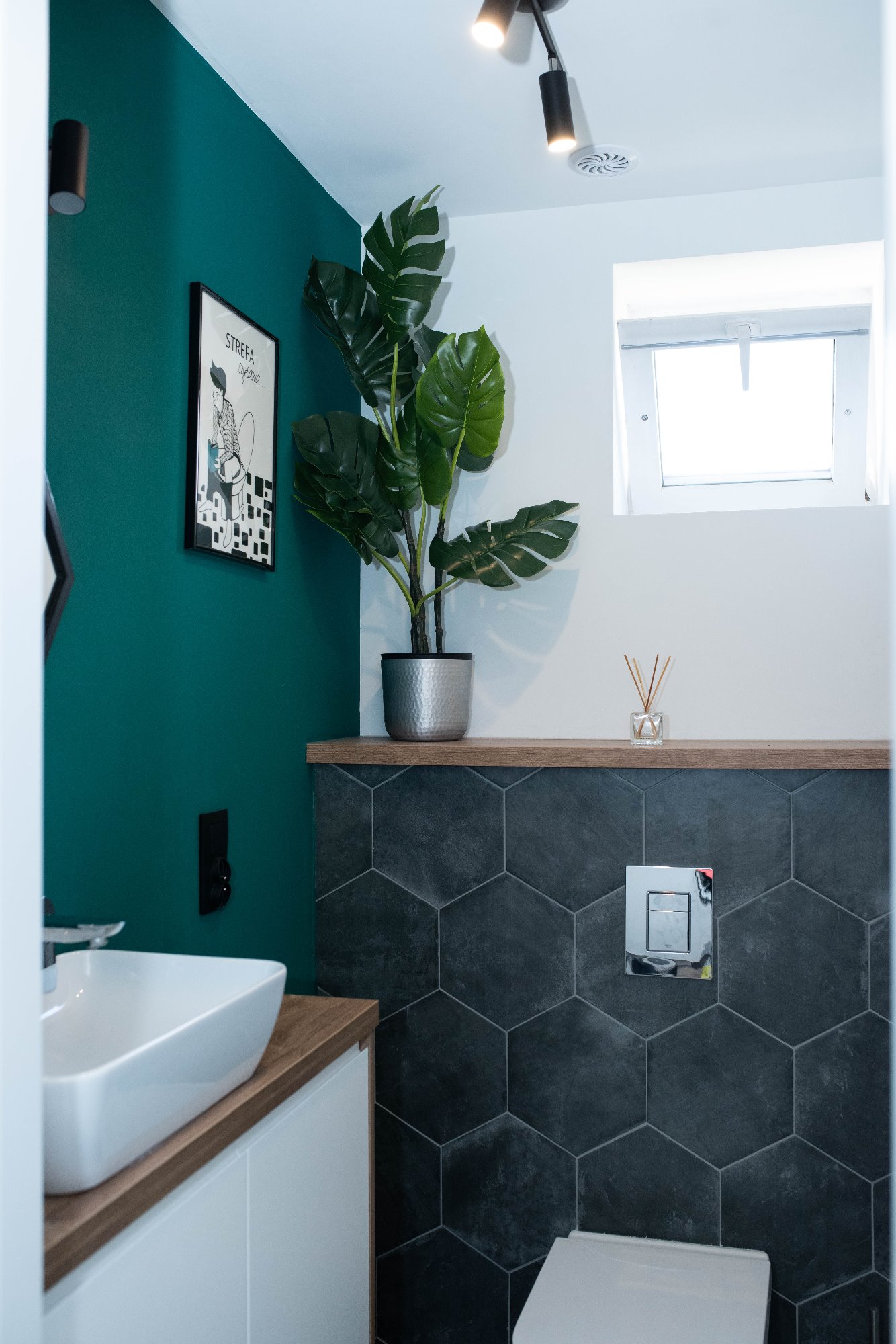 Nowoczesna łazienka w Gdańsku z turkusową ścianą, heksagonalnymi płytkami, białą umywalką nablatową i rośliną w srebrnej doniczce.