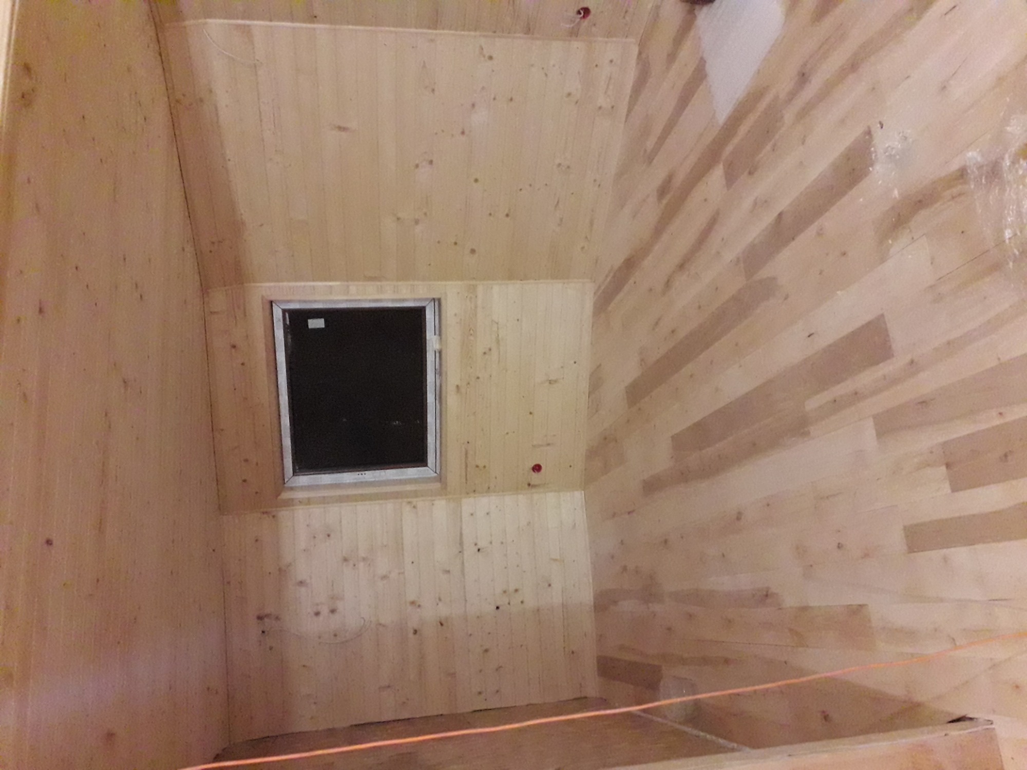 Poddasze wykończone boazerią z oknem, widoczne niedoskonałości montażu i ślady po pracach wykończeniowych.