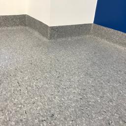 Floordeco - Szara, wzorzysta podłoga z listwami przypodłogowymi w rogu pomieszczenia z białymi i niebieskimi ścianami.