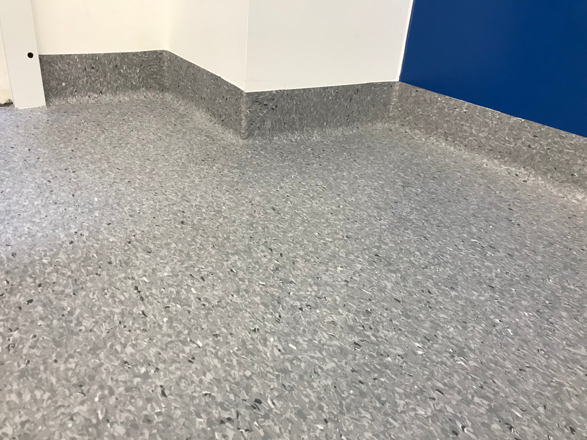 Szara, wzorzysta podłoga z listwami przypodłogowymi w rogu pomieszczenia z białymi i niebieskimi ścianami.