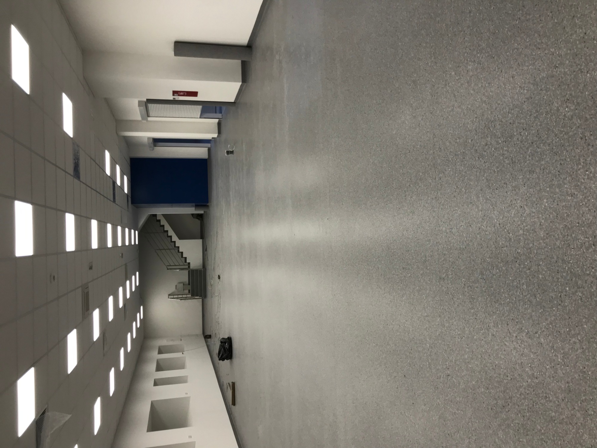 Korytarz biurowy z szarą wykładziną, widoczne schody i oświetlenie sufitowe