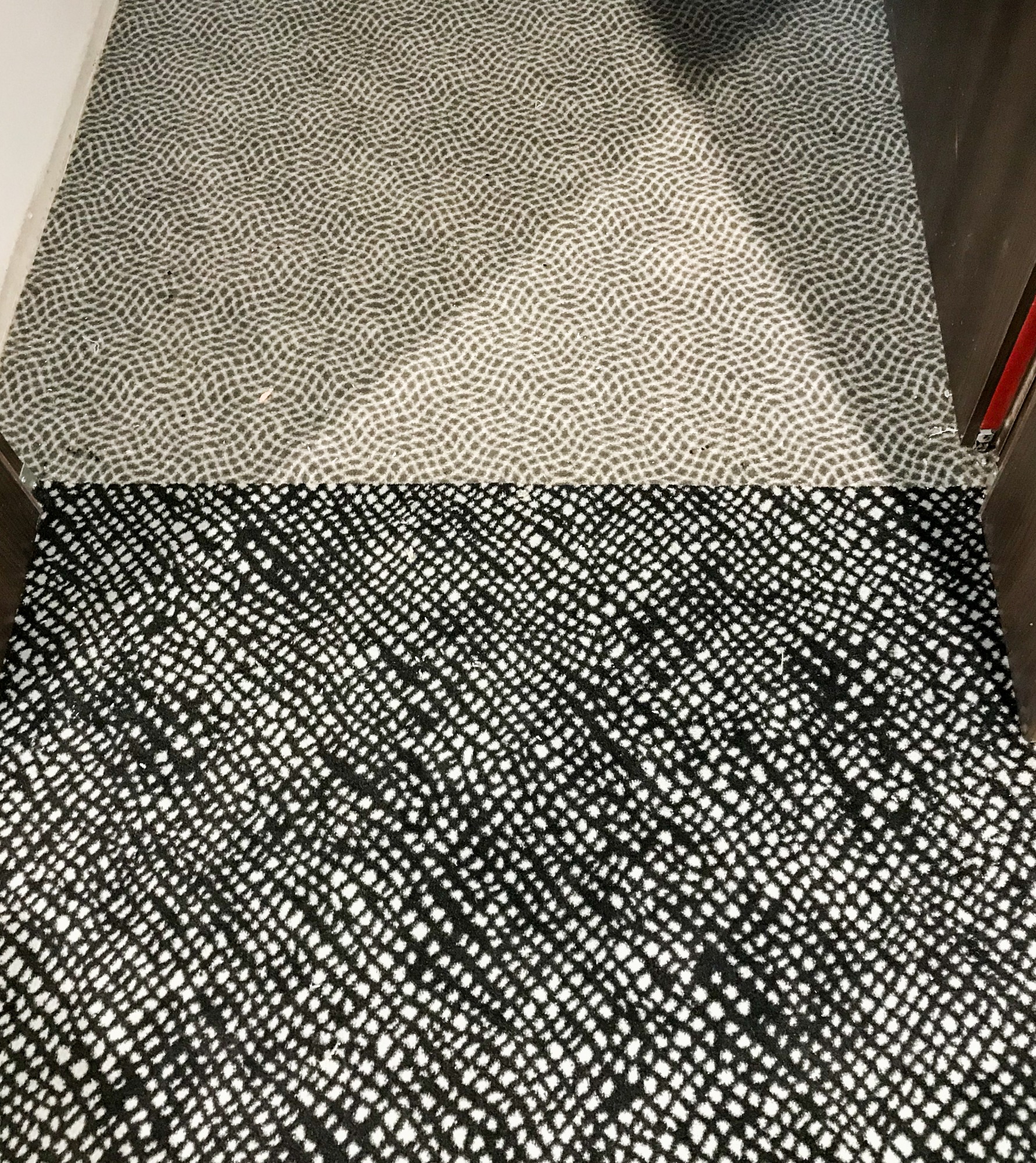 Fragment podłogi z dwoma rodzajami wzorzystej wykładziny: górna część szara z drobnym deseniem, dolna część czarno-biała z regularnym wzorem kratki.