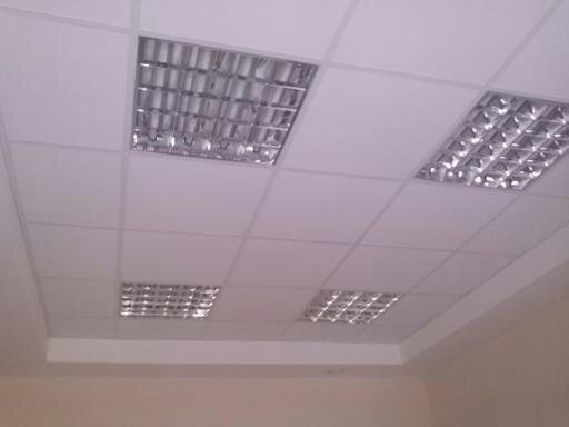 Sufit podwieszany z kwadratowymi panelami i wpuszczonymi lampami rastrowymi, widok z dołu, jasne pomieszczenie.