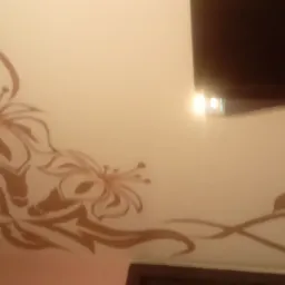 Dekoracyjny wzór kwiatowy w kolorze beżowym, namalowany na białym suficie, z fragmentem ciemnego elementu architektonicznego w tle.