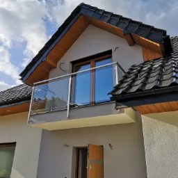 Nowoczesny balkon z szkła i stali nierdzewnej w nowym domu z ciemną dachówką, widok z dołu.