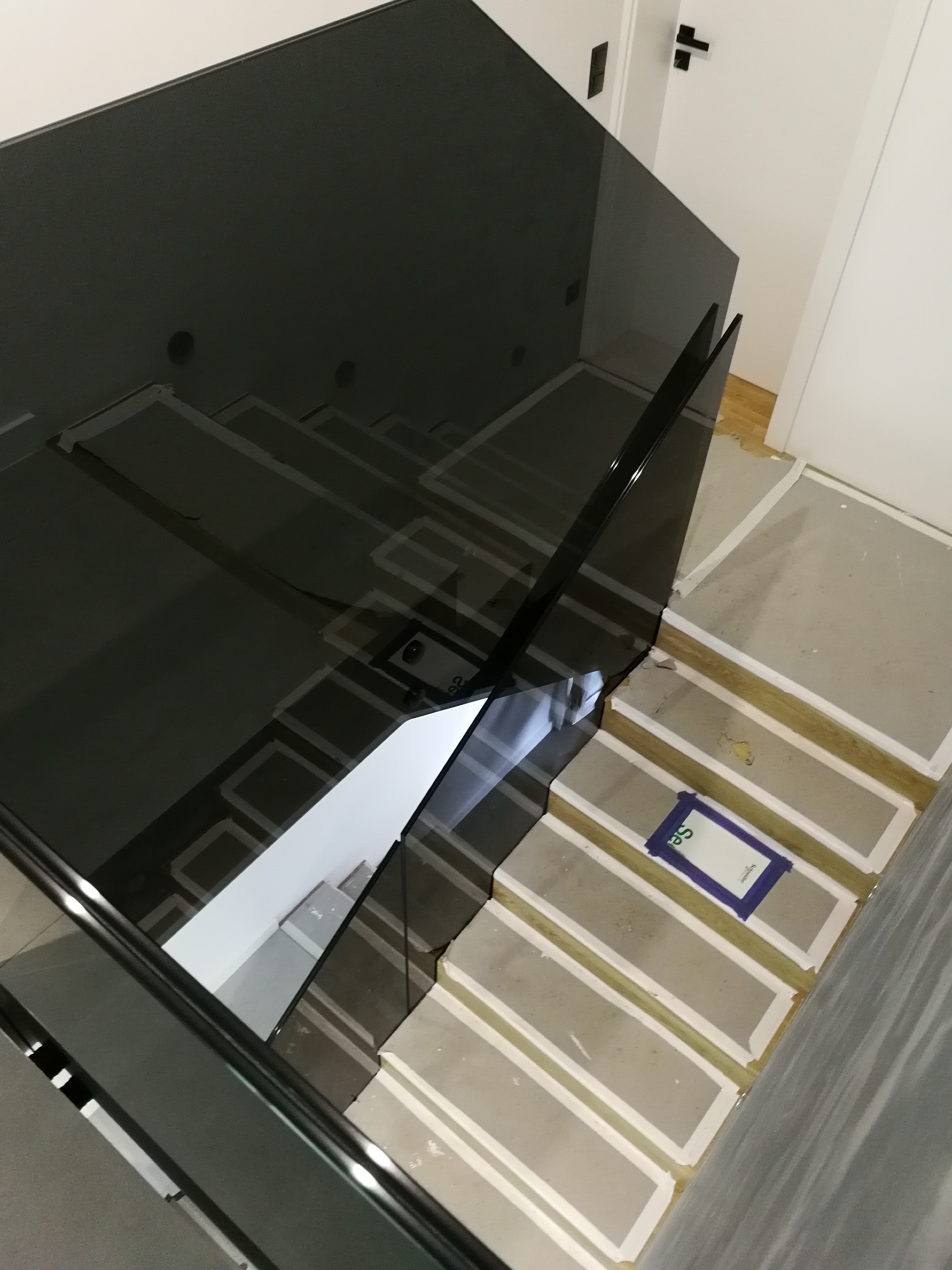 Wysoki kąt widzenia na schody w trakcie budowy z czarną szklaną balustradą, zabezpieczone taśmą malarską.