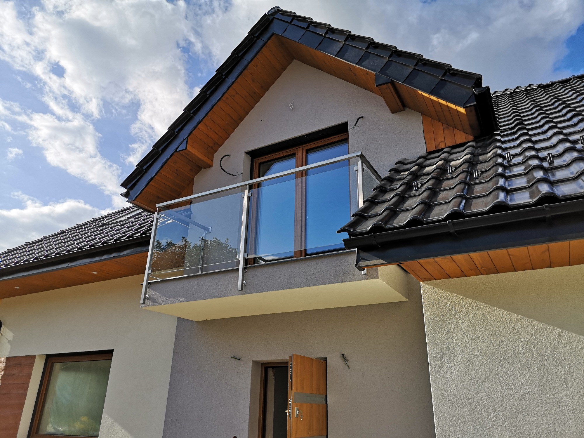 Nowoczesny balkon z szkła i stali nierdzewnej w nowym domu z ciemną dachówką, widok z dołu.