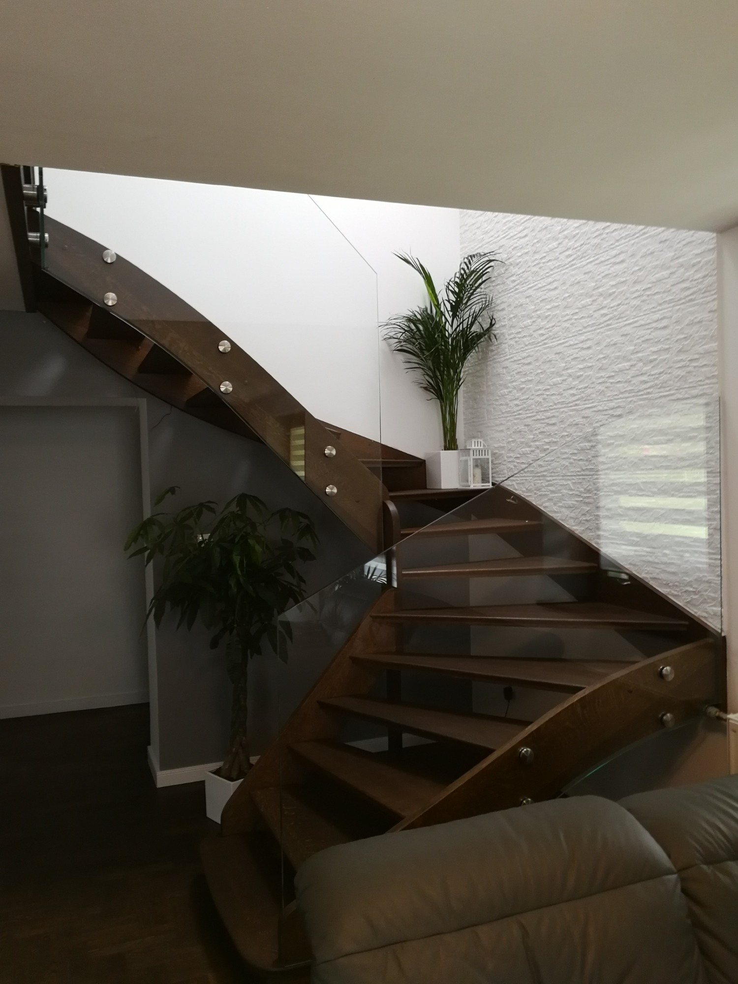 Drewniane schody z przezroczystą szklaną balustradą, mocowaną punktowo, z roślinami doniczkowymi jako element dekoracyjny w nowoczesnym wnętrzu.