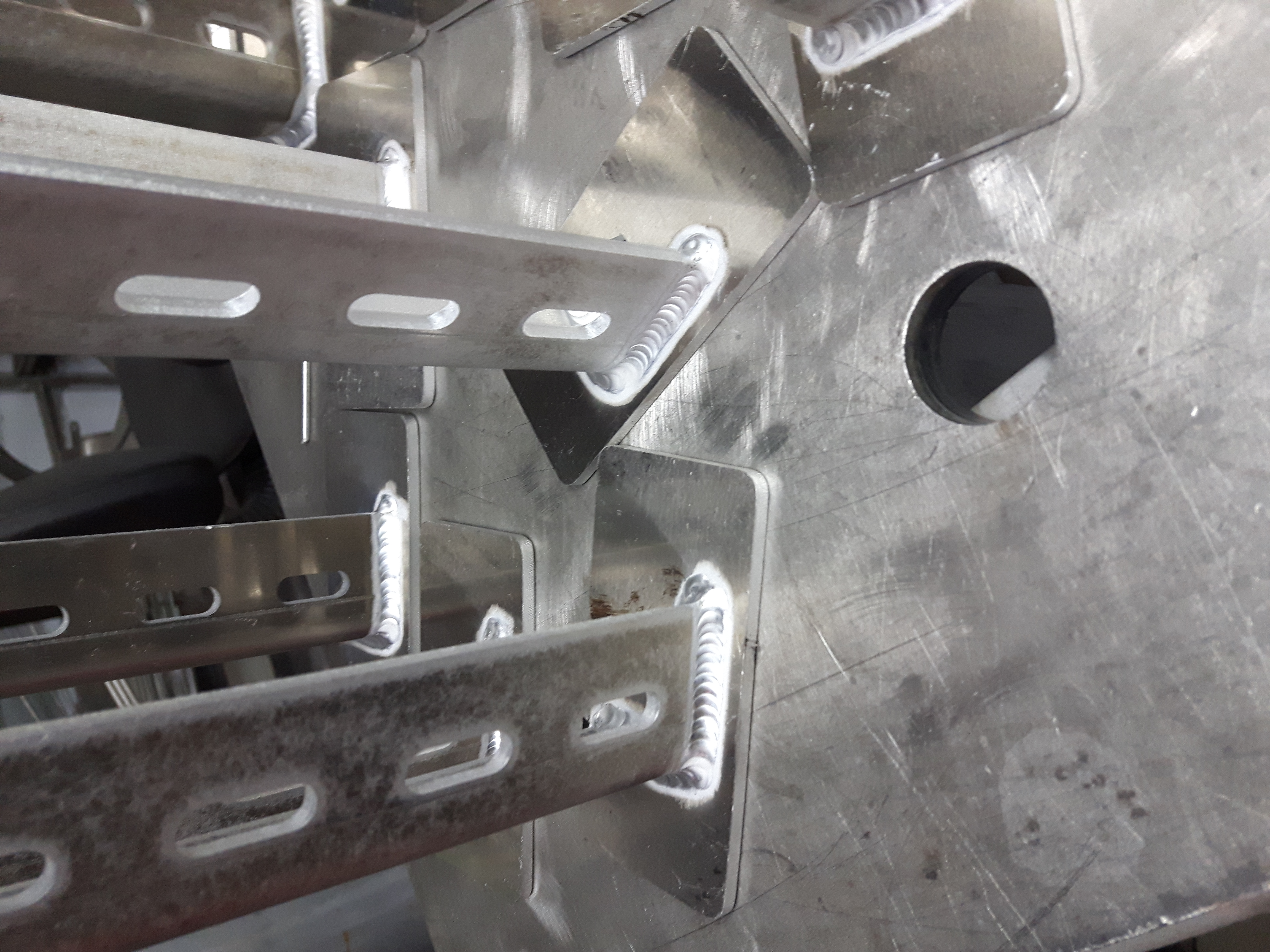 Szczegółowe zbliżenie spawanych, perforowanych metalowych profili, widoczne ślady obróbki i otwór w tle.