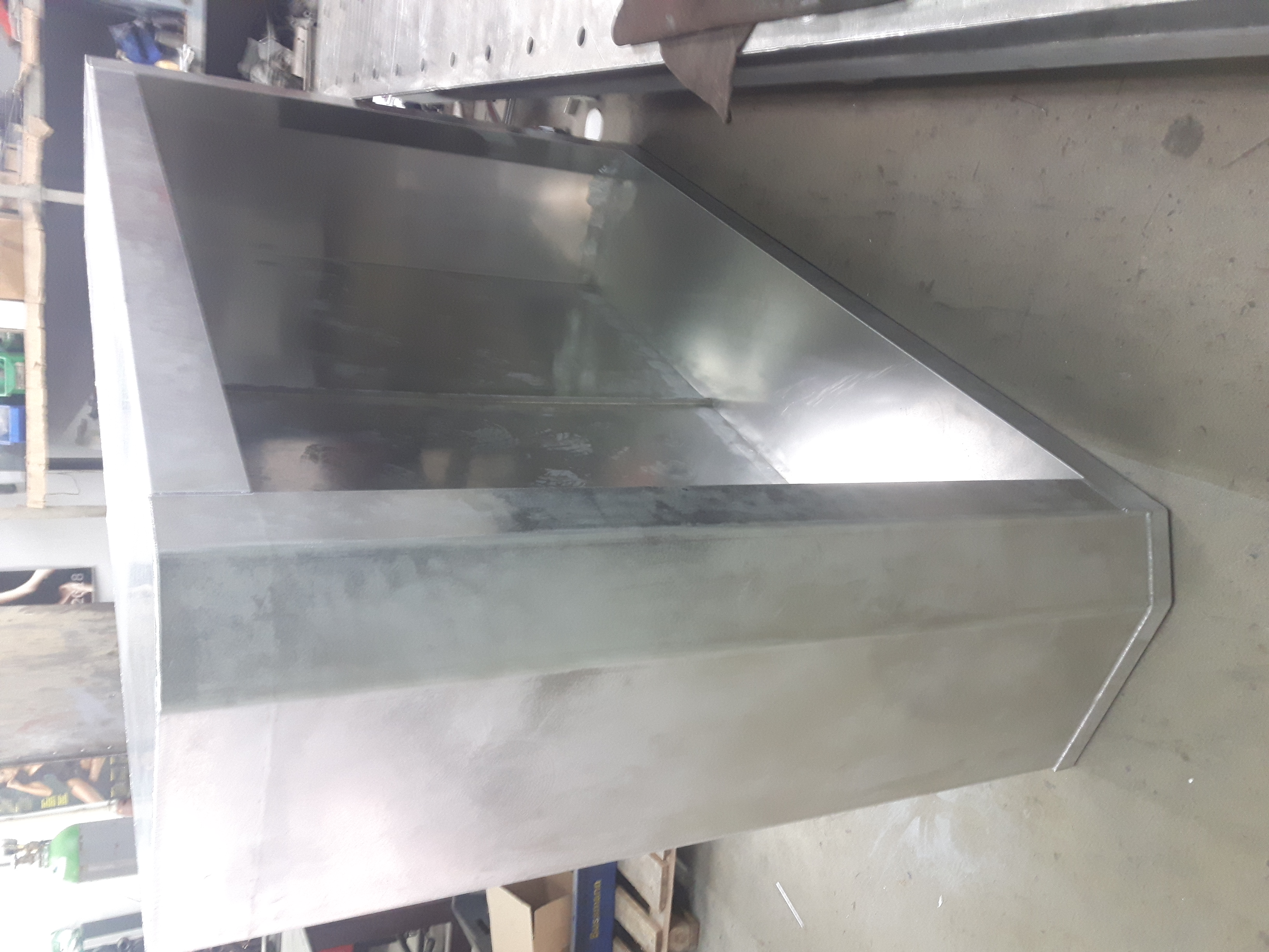 Surowy, metalowy element konstrukcyjny o kątowej budowie, prawdopodobnie fragment większej całości, widoczny w warsztatowym otoczeniu.