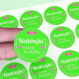 Arkusz z okrągłymi, zielonymi etykietami z napisem 'Naklejki różne kształty', trzymany w palcach.