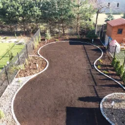 Przygotowany teren pod trawnik lub nasadzenia, obrzeża z jasnej kostki granitowej, widok z góry na posesję z metalowym ogrodzeniem i drewnianą altaną.