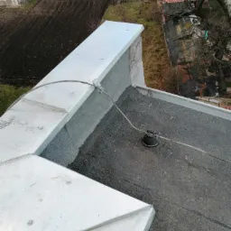 Widok z góry na fragment dachu pokrytego papą i obróbki blacharskie z blachy ocynkowanej, z widocznym systemem odgromowym w Dzierżoniowie.