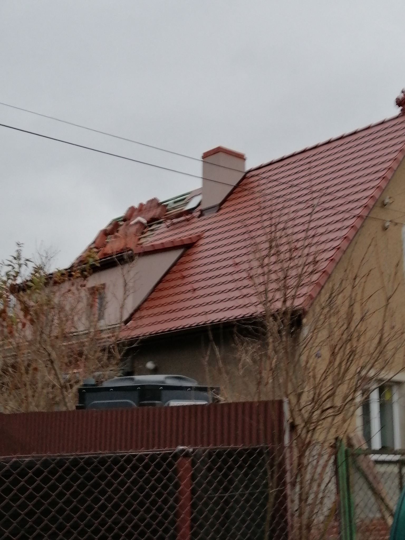 Dom z częściowo zdemontowanym dachem z czerwonej dachówki, widoczne uszkodzenia i brakujące elementy, przygotowanie do wymiany dachu.