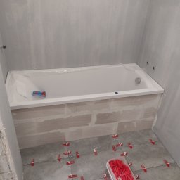 Tuszynski artur - Wanna obudowana cegłami, przygotowana do położenia płytek. Na podłodze ułożone płytki z użyciem czerwonych klipsów poziomujących. Ściany w trakcie przygotowywania pod wykończenie.