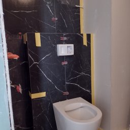 Tuszynski artur - Montaż podwieszanej toalety na tle marmurowych płytek w łazience w trakcie wykańczania, widoczne poziomice i taśma malarska.