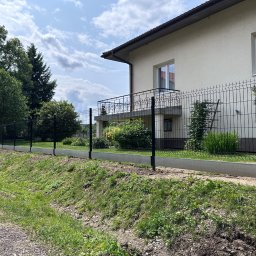 SEMAX Andrzej Sech - Nowoczesne ogrodzenie panelowe w kolorze grafitowym, zamontowane na betonowej podmurówce, otacza posesję z zielonym trawnikiem i domem w tle.