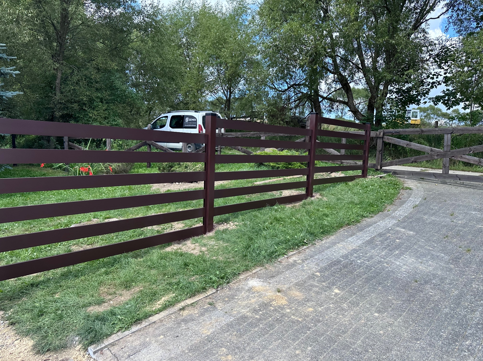 Nowoczesne, poziome ogrodzenie panelowe w kolorze brązowym, z widoczną bramą w tle i firmowym vanem. Estetyczne wykończenie posesji.
