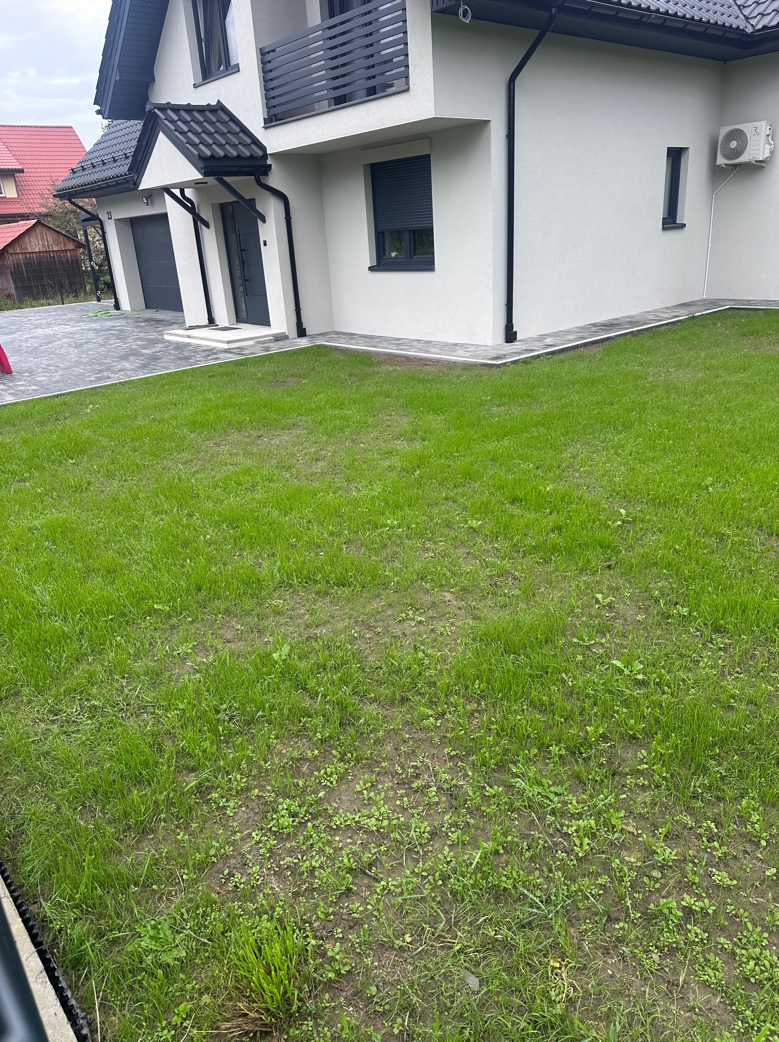 Nowoczesny dom jednorodzinny z szarą kostką brukową, widok z trawnika. Minimalistyczna architektura z elementami w kolorze grafitowym.