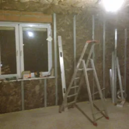 Montaż izolacji z wełny mineralnej na poddaszu w Biedaczowie, widoczne metalowe profile, drabina, poziomica i narzędzia na parapecie okna.