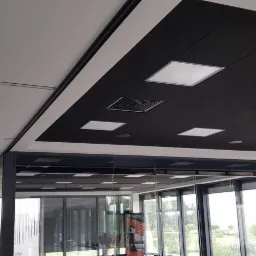 Dwukolorowy sufit podwieszany z wbudowanym oświetleniem i systemem wentylacji w nowoczesnym biurze z przeszkleniami.