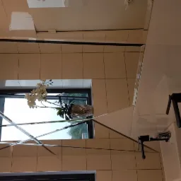 Nowoczesna łazienka w Ostrowie Wielkopolskim z jasnymi płytkami, lustrami w geometryczne wzory, dekoracyjnym oświetleniem i umywalkami z czarną armaturą.