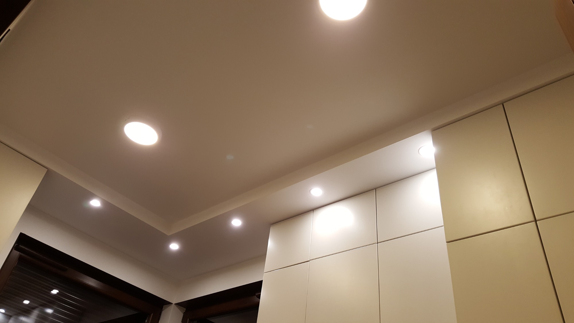 Jasny, gładki sufit z wbudowanymi punktowymi lampami LED, widoczne fragmenty zabudowy meblowej w kolorze kremowym.