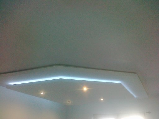 Biały sufit podwieszany z oświetleniem LED w kształcie litery L i trzema punktowymi lampami halogenowymi.