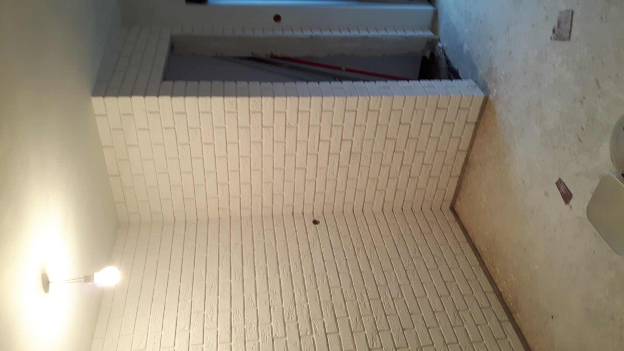 Świeżo pomalowana na biało ściana z cegły dekoracyjnej, widok od dołu, z widocznym otworem w ścianie i surową podłogą w tle.