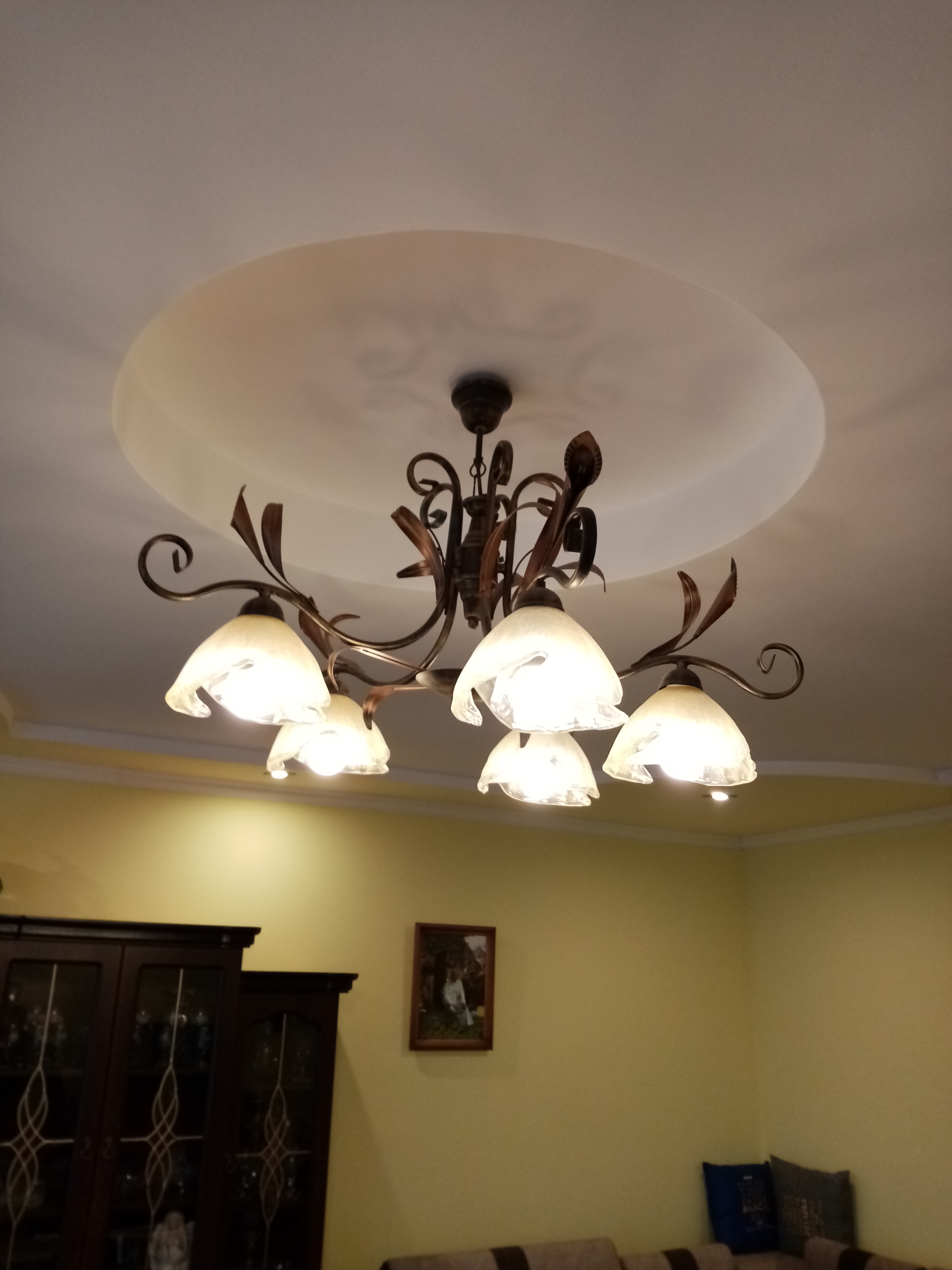 Żyrandol z sześcioma szklanymi kloszami w kształcie kwiatów zamontowany na suficie z okrągłym podwieszanym elementem dekoracyjnym.