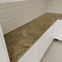 Wykończony blat kuchenny z granitu Milenium Fantasy o falującej strukturze, zamontowany na białych szafkach kuchennych, z białymi płytkami na ścianie.