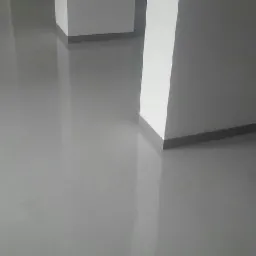 Gładka, szara posadzka żywiczna w pomieszczeniu z białymi, kwadratowymi kolumnami, widoczne odbicia światła na podłodze.