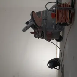 Szlifierka do gładzi gipsowych z odkurzaczem przemysłowym na tle ściany z widocznymi łatami gipsowymi.