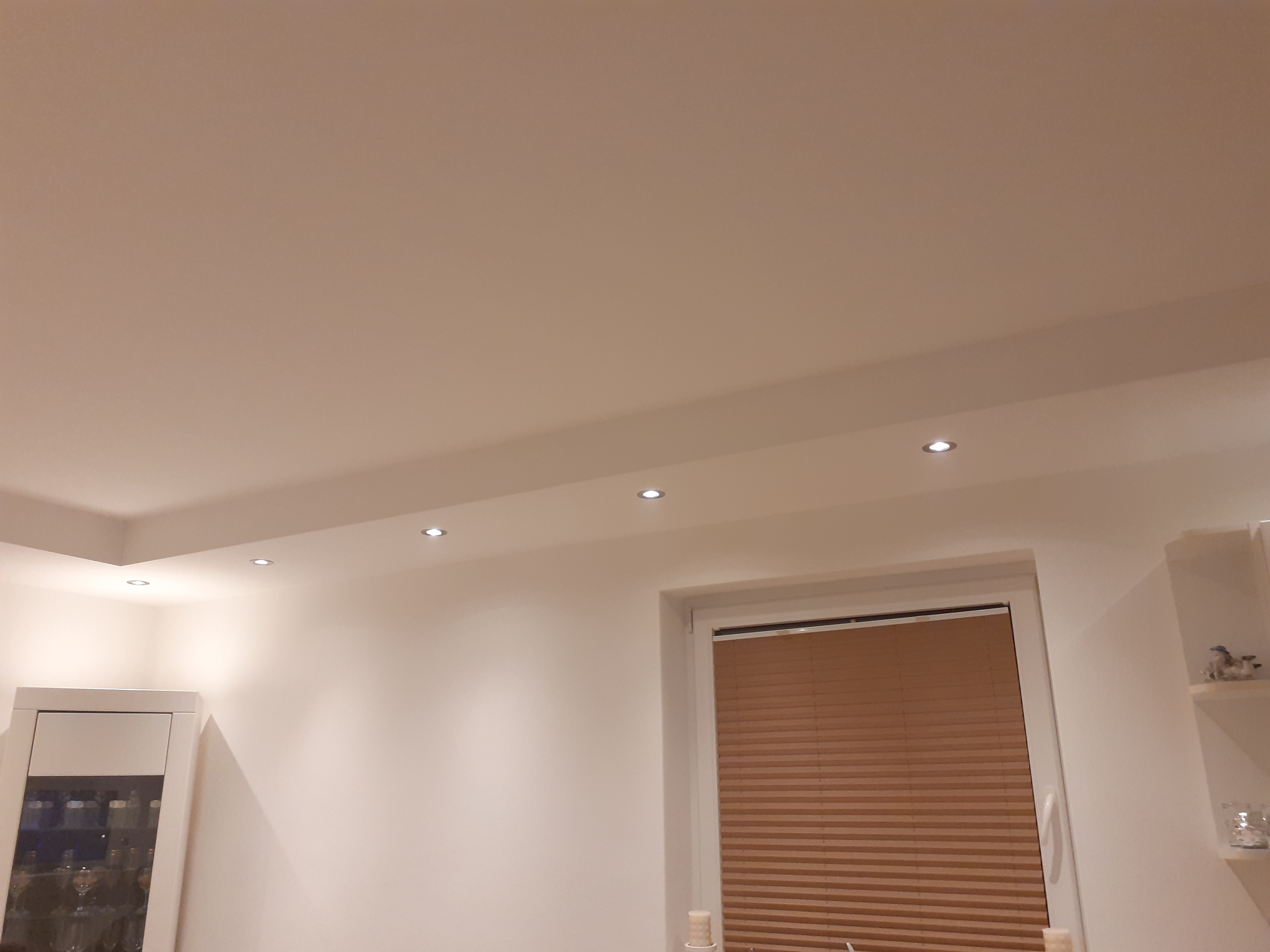 Jasne wnętrze po remoncie z równo pomalowanymi ścianami, oświetleniem punktowym w suficie podwieszanym i oknem z żaluzjami plisowanymi.