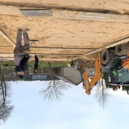 Przygotowanie terenu pod fundamenty: pracownicy z łopatami i koparka Case 580ST na placu budowy, widoczne wyznaczone granice fundamentów i podsypka piaskowa.