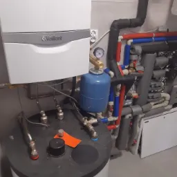 Kocioł gazowy Vaillant z podłączonym zasobnikiem ciepłej wody i rozbudowaną instalacją hydrauliczną z rurami w izolacji, manometrem i zaworami.