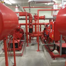 Kompleksowa instalacja przeciwpożarowa z czerwonymi rurami, zbiornikami i silnikami, widok na system w pomieszczeniu technicznym.