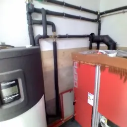 Kotłownia z piecem na paliwo stałe Defrö i zasobnikiem Buderus, widoczne rury w izolacji i elementy instalacji.