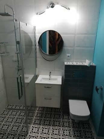 Nowoczesna łazienka z kabiną prysznicową, okrągłym lustrem i wzorzystą podłogą w odcieniach szarości.