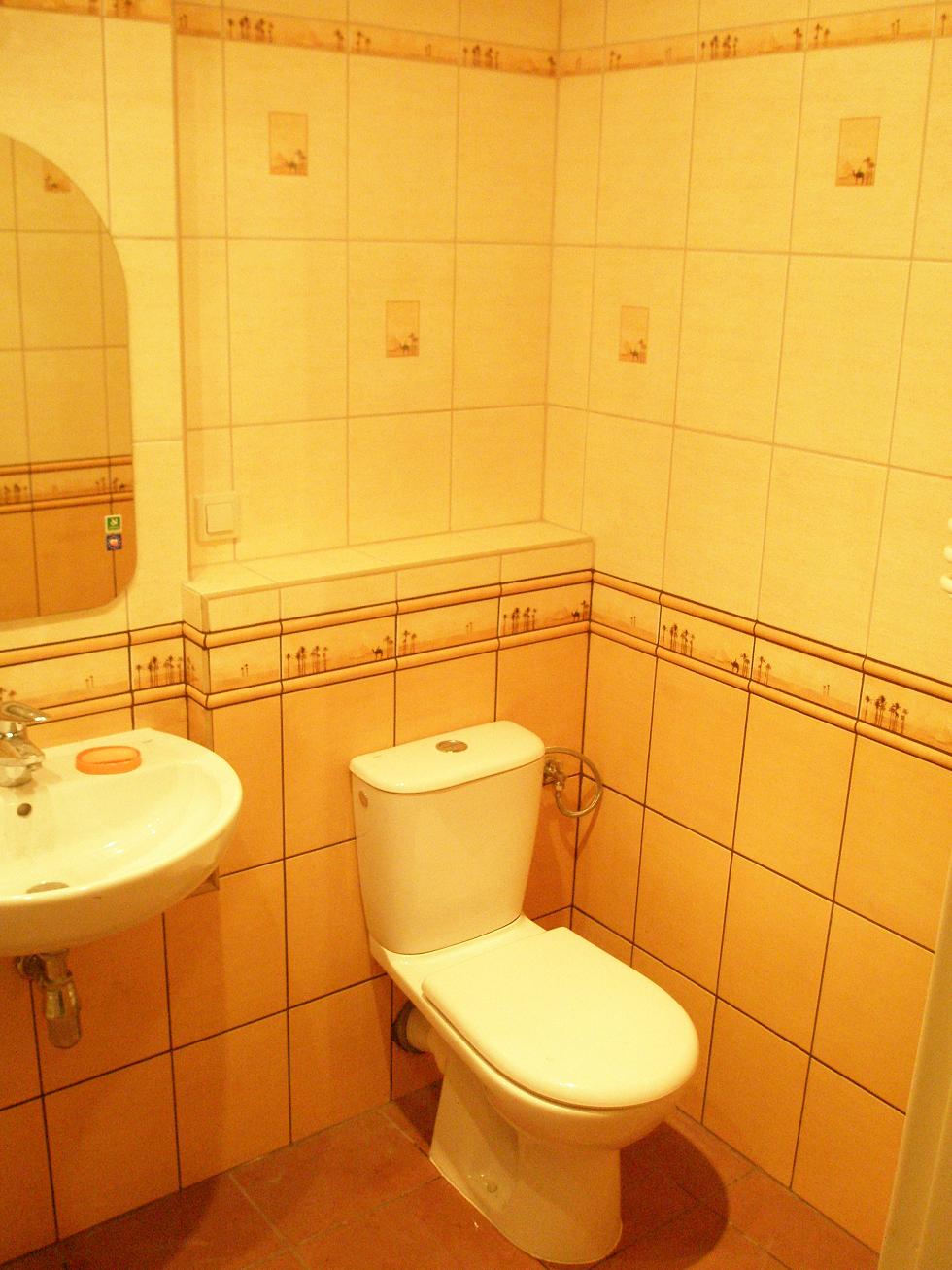 Ukończona łazienka z żółtymi płytkami, umywalką na ścianie i toaletą, dekoracyjne bordiury z motywem pustynnym.