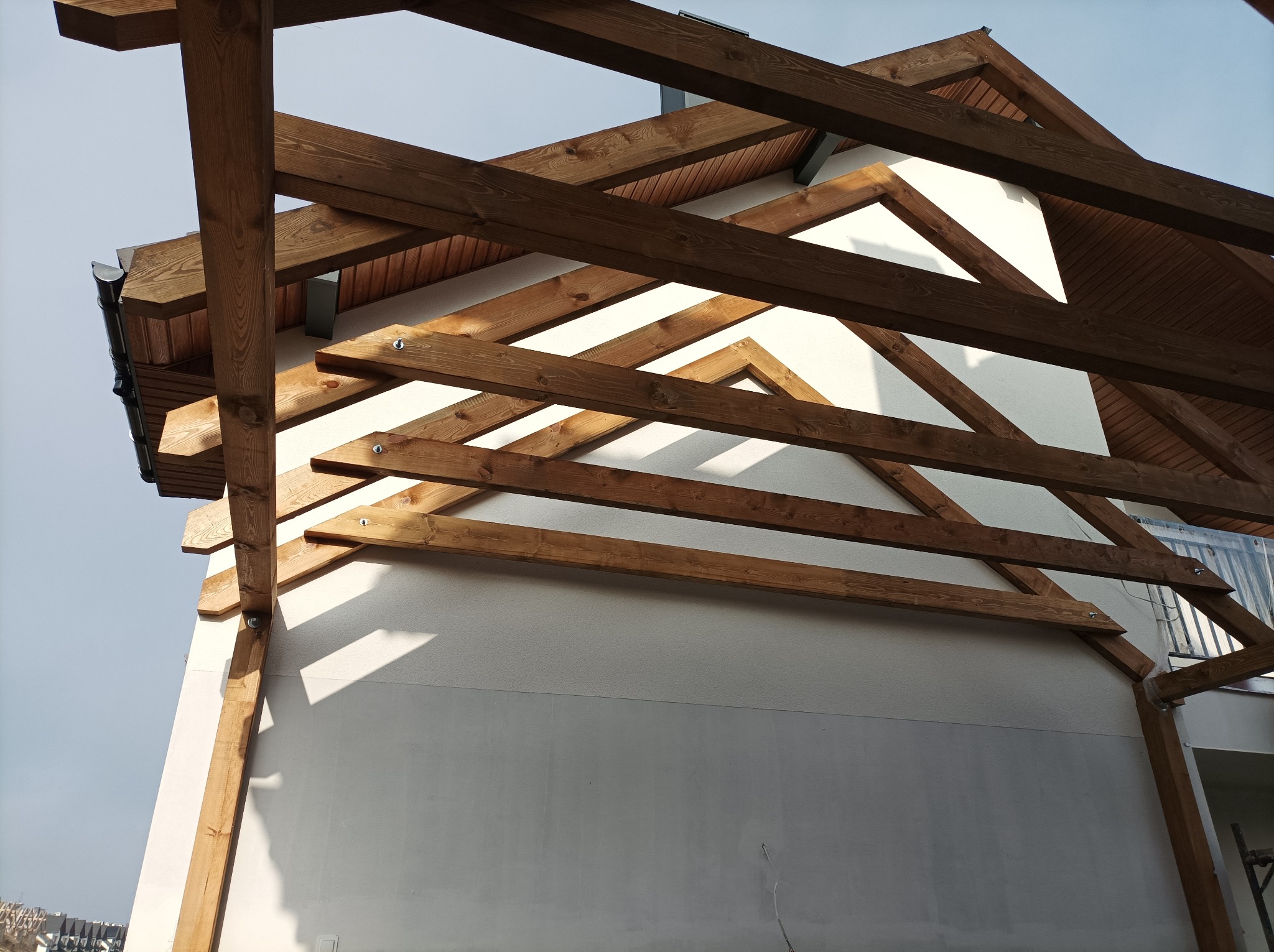 Konstrukcja dachu domu szkieletowego z widocznymi drewnianymi belkami i elementami mocującymi, ujęcie z dołu.