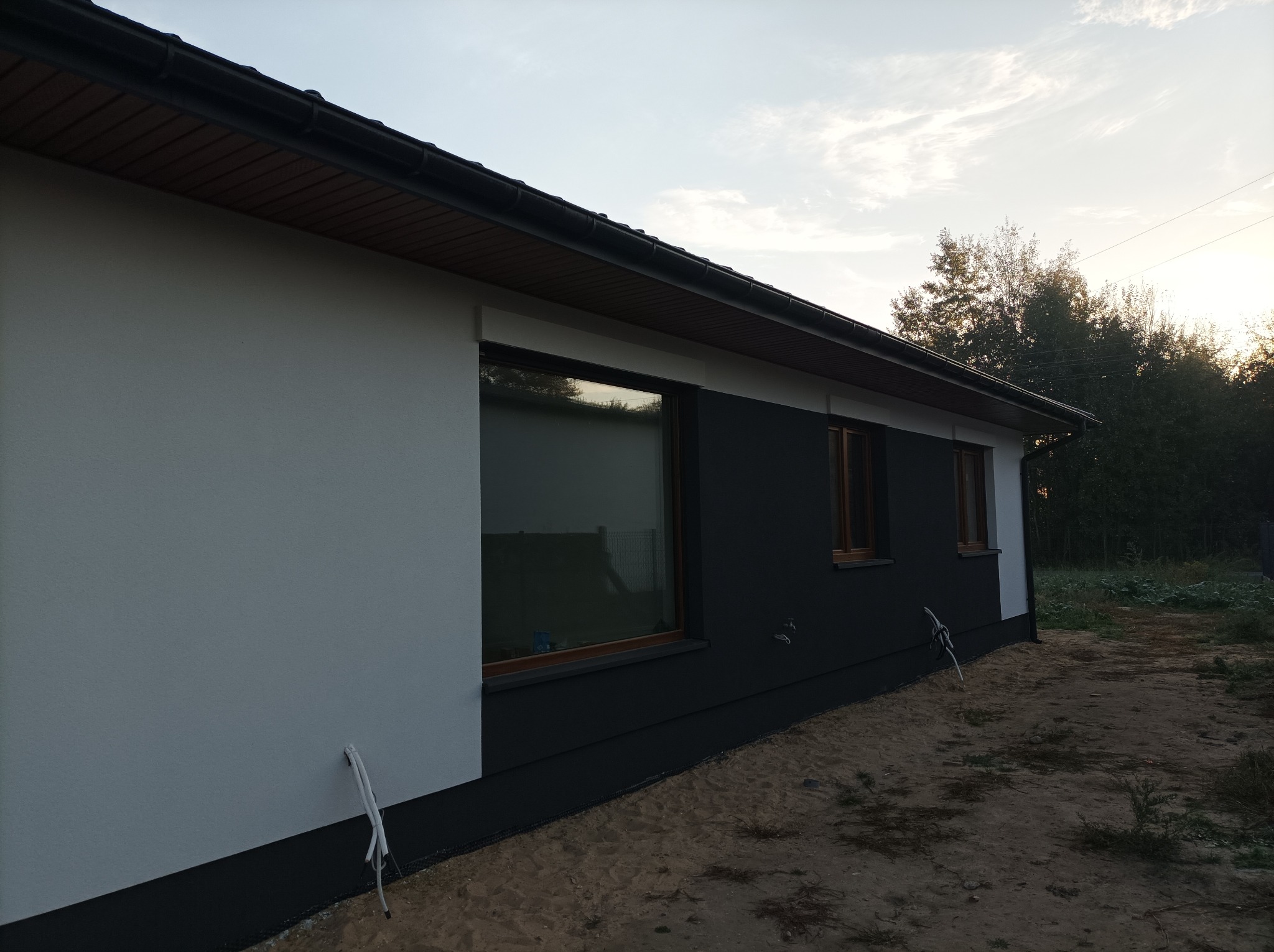 Dwukolorowa elewacja domu z drewnianą stolarką okienną, widok z boku, przewody wystające ze ściany.