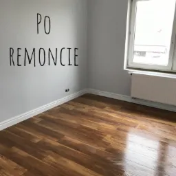 Pusty pokój po remoncie z nową, błyszczącą podłogą z paneli drewnopodobnych, szare ściany z napisem 'PO REMONCIE' i białą listwą przypodłogową, okno z grzejnikiem.