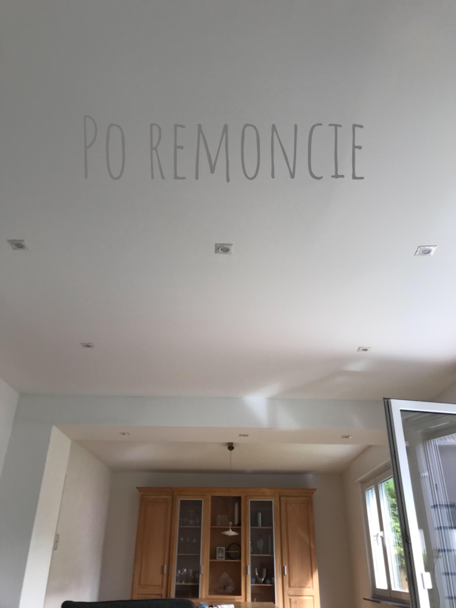 Biały sufit z zamontowanymi kwadratowymi lampami LED po remoncie, widok na drewnianą witrynę i okno w tle.