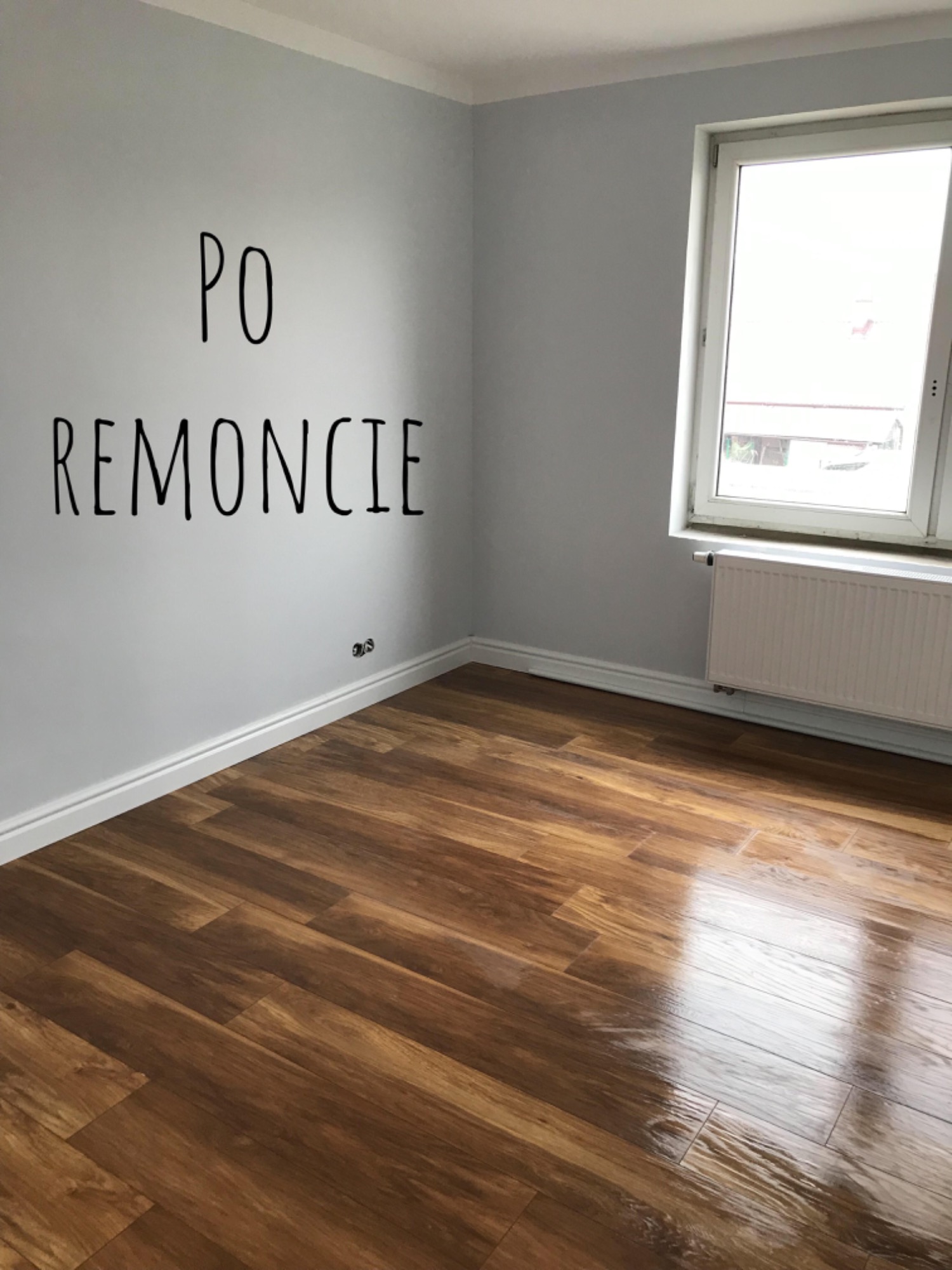 Pusty pokój po remoncie z nową, błyszczącą podłogą z paneli drewnopodobnych, szare ściany z napisem 'PO REMONCIE' i białą listwą przypodłogową, okno z grzejnikiem.