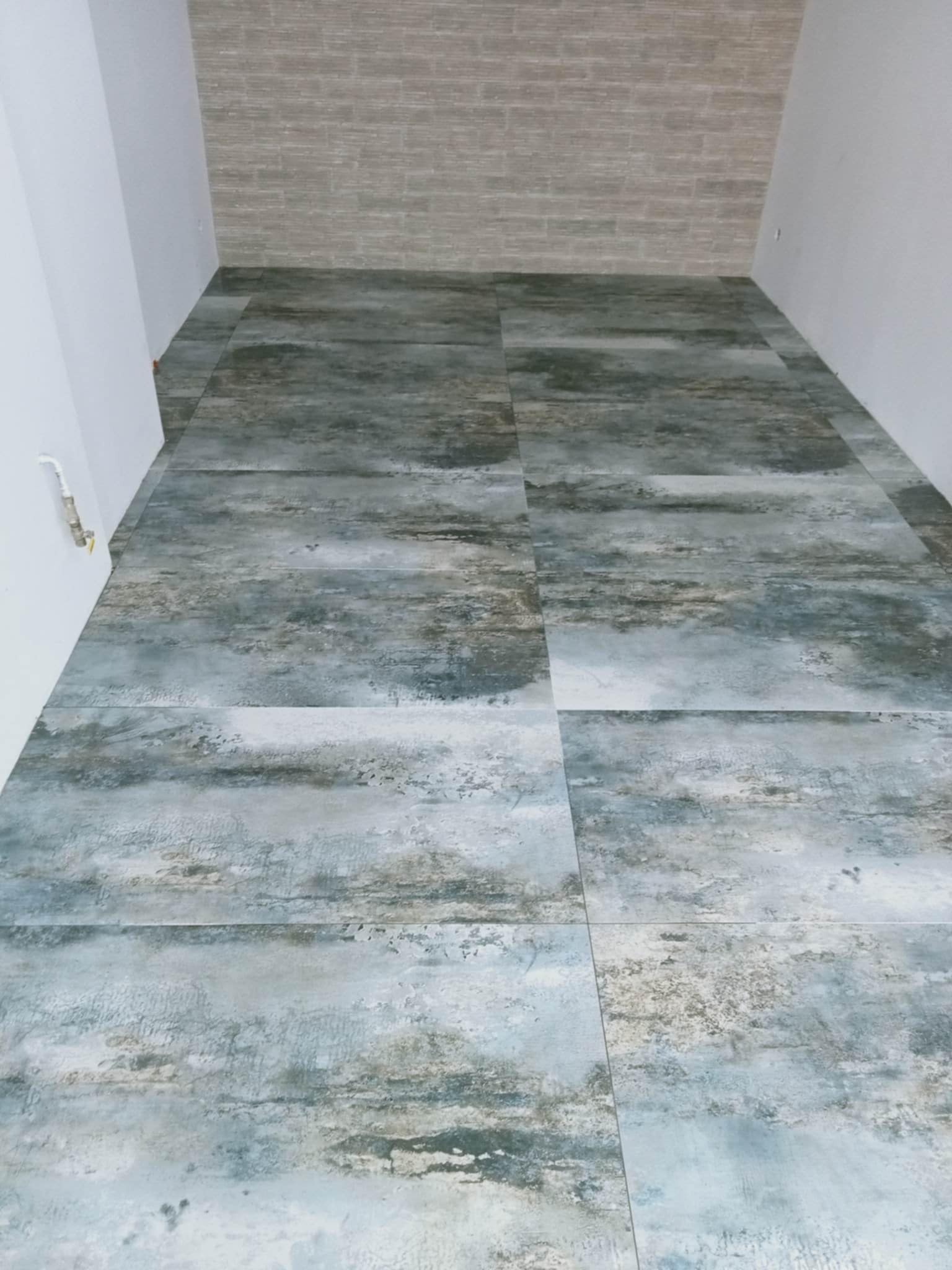 Ułożona podłoga z płytek imitujących kamień w pomieszczeniu w Kargowej, z fragmentem ściany wyłożonej cegiełkami.