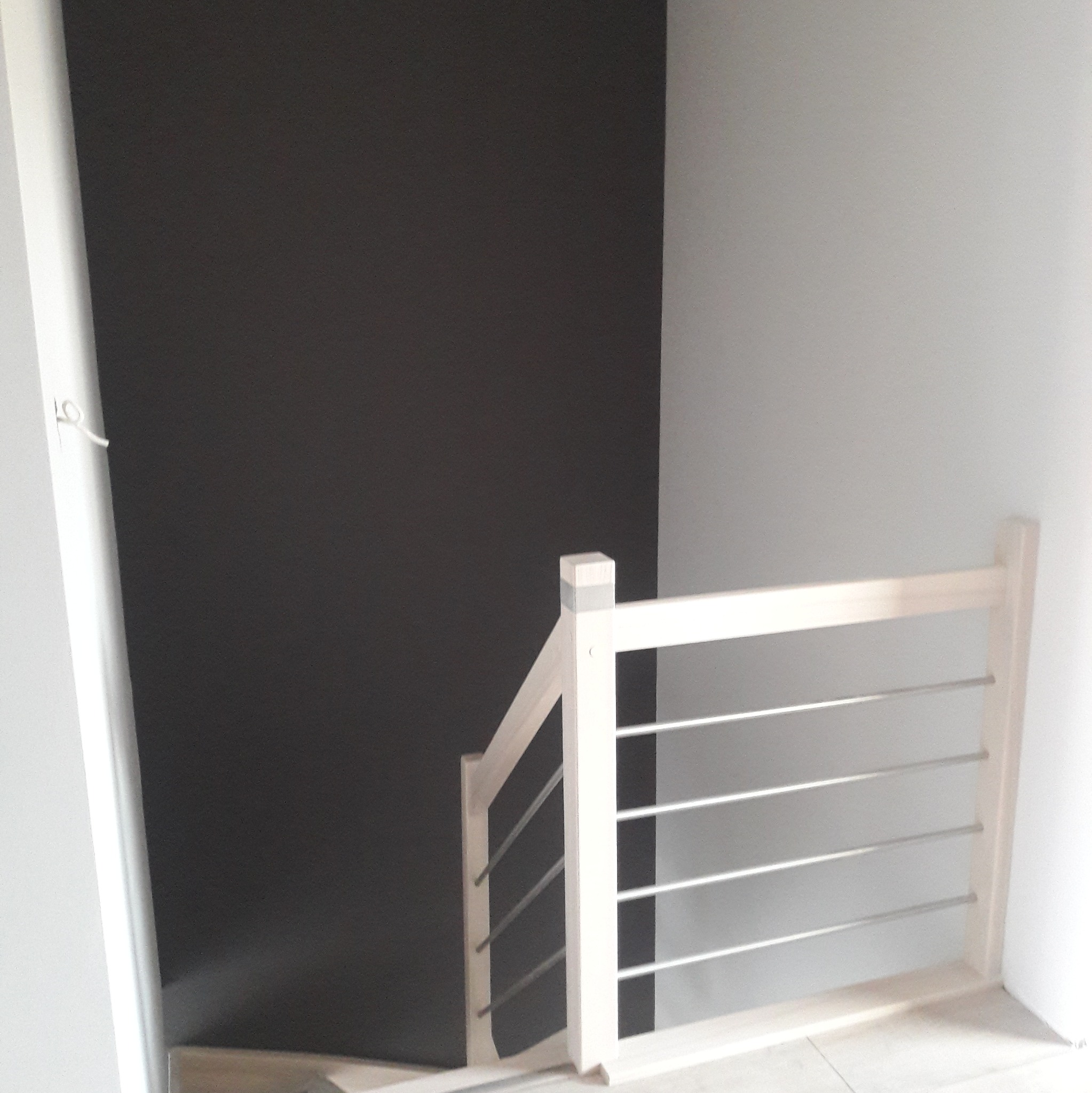 Fragment wykończonej klatki schodowej z białą balustradą z poziomymi, metalowymi prętami na tle ciemnoszarej ściany.