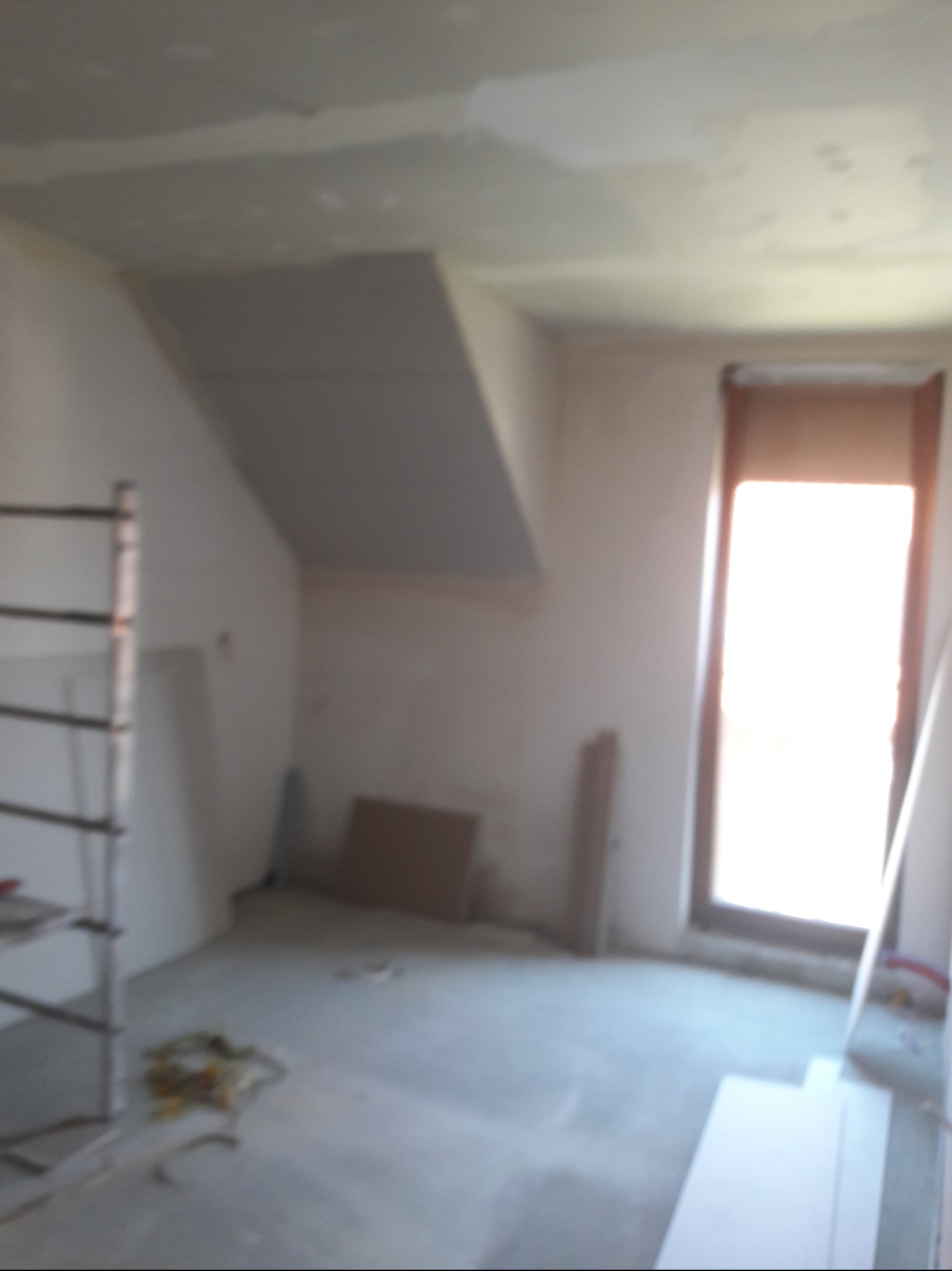 Wnętrze pokoju w Lubinie w trakcie montażu płyt kartonowo-gipsowych na skośnym suficie, widoczny fragment rusztowania i materiały budowlane